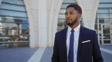 Takım elbiseli genç Afro-Amerikan bir adam şehir merkezinde dikiliyor.