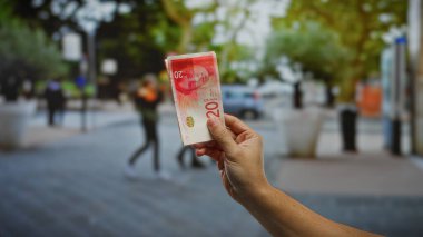 İsrail Şekel 'i elinde tutan adam şehir sokaklarında finans kavramlarını ve yatırım fırsatlarını gösteren banknotlar tutuyor..
