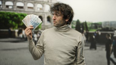 Roma Kolezyumu 'nun önünde elinde Polonya parası tutan adam Roma caddesinde kültürel ve finansal zıtlık sergiliyor..