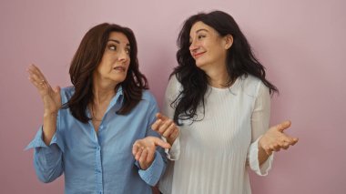 İki orta yaşlı kadın pembe bir arkaplanda durmuş gülümsüyor ve el kol hareketi yapıyor, kardeşçe bir bağ ve dostluğu resmediyor..