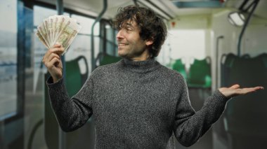 Hispanik bir adam otobüsün içinde kendine güvenen bir gülümsemeyle Rus rublesini tutuyor. Toplu taşıma ortamında zenginliği ve başarıyı vurguluyor. Sıradan bir tarz sergiliyor..
