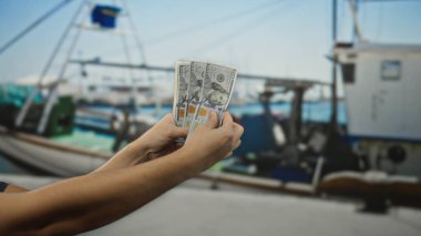 Deniz kıyısında tekneli Amerikan banknotlarını tutan adam güneşli açık hava ortamında sakin su, sergilenen seyahat ve finans konsepti..