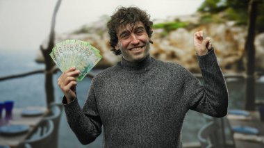 Sahil sahilinde elinde rusya rublesi tutan gülümseyen bir adam. Neşeli bir ifade takınıyor. Servet ve eğlence sergiliyor..