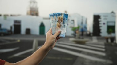 Şehir caddesinde elinde İsviçre frangı banknotları tutan adam arka planda hareket eden insanlarla şehir manzarası tasvir ediyor..
