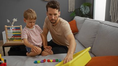 Baba ve oğul evde rahat bir oturma odasında eğitici oyuncaklarla oynayıp öğreniyorlar.