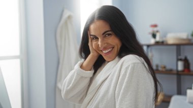 Arka planda güzellik ürünleri ve sağlık ürünleri olan bir spa odasında gülümseyen kadın.