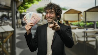 İspanyol bir adam, şehir sokaklarında elinde Thai banknotları tutan kamerayı göstererek açık hava kentsel ortamında kendine güvenini gösteriyor..