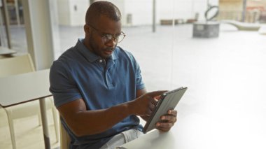 Bir ofiste tablet kullanarak çalışan yakışıklı Afro-Amerikalı adam modern bir iş ortamındaki görevine odaklandı.