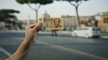 Macar banknotlarını elinde tutan adam işlek bir şehir caddesinde şehir manzarasını ve günlük hayatı yakalıyor..