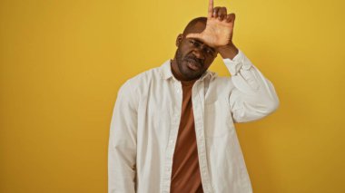 İzole edilmiş sarı arka planda poz veren genç bir adam ciddi bir ifade takınarak alnında ezik işareti yapıyor..