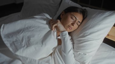 Genç bir kadın yatak odasında uyuyor. Yüzünde barışçıl bir ifade ve vücudunu örten bir battaniye var.