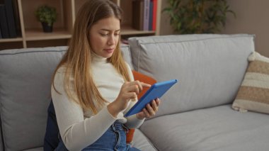 Modern koltukta tablet kullanan genç bir kadın şık bir apartman dairesinde rahat bir dekor içinde evinde rahat teknoloji yaşam tarzını sergiliyor..
