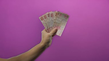 Bir adamın elinde Türk lirası banknotlar canlı mor bir duvar arkaplan gösterme para birimi ve finansal kavramlar karşı.