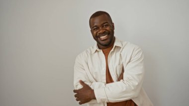 Çapraz kollu yakışıklı adam, parlak beyaz bir arka plana karşı güvenle gülümsüyor rahat ve cana yakın bir tavır sergiliyor..