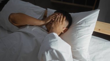 Yatakta uzanırken yüzünü ellerle kaplayan genç adam, bir sabah uyanıklığı ya da rahat bir yatak odası ortamında derin düşünceleri akla getiriyor..