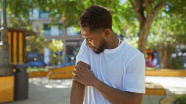 Beyaz tişörtlü genç adam güneşli bir günde şehir parkında kolunu kaşıyordu.