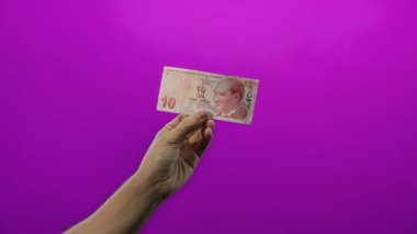 Canlı mor bir zemin üzerinde Türk lira banknot tutan adam, basit ve izole bir ayar ile para birimini vurguluyor.
