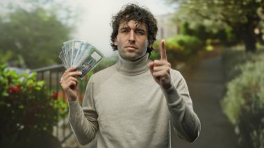 Bangladeshi Taka 'yı bir park ortamında elinde tutan İspanyol bir adam. Odaklanmış bir ifadeyle, açık havada yemyeşil para birimini vurguluyor..