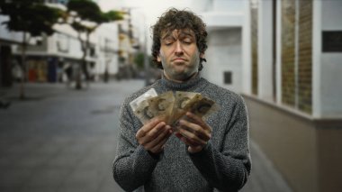 Hispanik bir adam elinde İngiliz sterlinlerinin banknotlarıyla şehir sokaklarında duruyor. İçerik bir ifadeyle finansal başarıyı ve şehir yaşam tarzını sembolize ediyor..