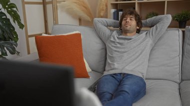 Genç İspanyol adam evdeki koltukta dinleniyor. Rahat bir oturma odasında, modern bir iç mekan ve rahat bir ortam içinde. Çekici bir yaşam tarzı sergiliyor..