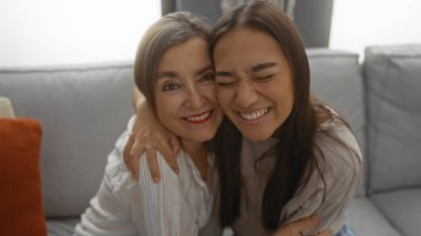 Anne ve kızı sıcak bir oturma odasında kanepede otururken sevgi dolu bir kucaklaşmayı paylaşıyorlar..