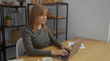 Ofis ortamında dizüstü bilgisayarda çalışan bir kadın, raflar, belgeler ve ahşap masadaki kahveyle modern çalışma ortamını sergiliyor..