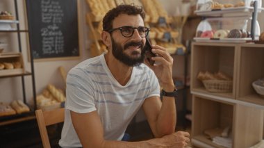Kapalı bir pastanede telefonda konuşan sakallı yakışıklı bir adam.