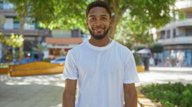 Şehir parkında gülümseyen yakışıklı genç bir adam..