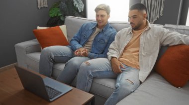 Modern bir oturma odasında rahatlayan arkadaşlar, iki yakışıklı adam bir dairede rahat bir kanepede dizüstü bilgisayar izliyor..
