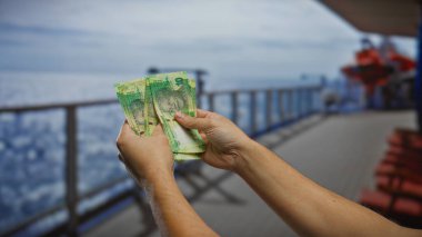Güney Afrika Rand 'ini elinde tutan adam arka planda deniz ve şehir manzarası olan bir teknede iş ve seyahat temalarını yakalıyor..