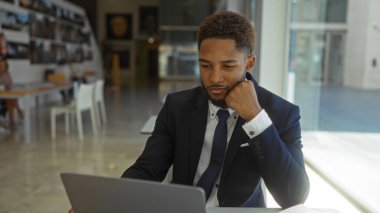 Genç bir adam modern ofis içinde dizüstü bilgisayarda çalışıyor. Parlak doğal ışığı var.