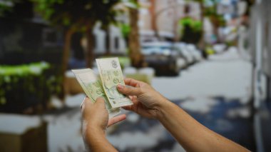 Kentsel bir caddede elinde tekil dolar tutan bir adam, açık havada döviz kuruna odaklı bir iş ya da yatırım senaryosunu vurguluyor..