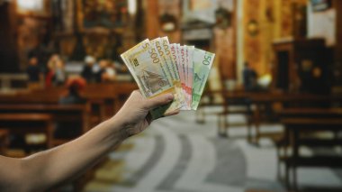 Elinde Norveç kronu banknotları tutan adam kilisenin içinde, arka planda insanların olduğu dini bir ortamda para sergiliyor..