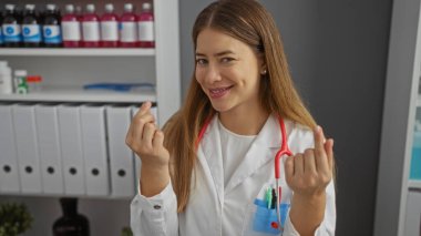 Klinik ortamında güvenle gülümseyen bir kadın steteskop ile laboratuvar önlüğü giyiyor modern bir hastane çalışma alanında rafları ve tıbbi malzemelerle profesyonellik gösteriyor..