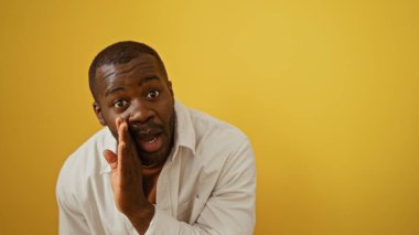 Genç adam, entrika ve iletişim duygusunu resmeden, parlak sarı bir arka plana karşı gizli bir jest yapıyor..