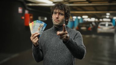 Kapalı otoparktaki İspanyol adam İsviçre franklarını elinde tutuyor. Güvenle işaret ediyor. Yapay ışık altındaki kentsel başarı ve zenginliği sembolize ediyor..