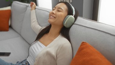 Evdeki kanepede dinlenen, kulaklık takan, müzikten zevk alan, içerideki huzurlu anı yansıtan bir gülümseme ile....