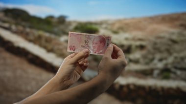 Elinde bir park zeminine karşı Türk lirası banknot tutan bir adam, gayri resmi ve doğal bir şekilde açık hava finans kavramlarını vurguluyor..