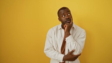 Genç Afrikalı Amerikalı adam sarı arka planda izole edilmiş, derin derin düşünüyor ve düşünceli görünüyor..