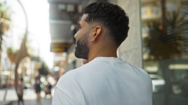 Güneşli bir günde şehirde şehir sokağında yürüyen sakallı çekici bir genç adam.