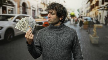 Amerikan doları banknotları tutan İspanyol adam hareketli bir şehir caddesinde duruyor, canlı bir ortamda finansal başarıyı ve şehir yaşam tarzını somutlaştırıyor..