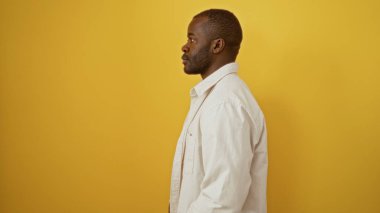 Yakışıklı, Afro-Amerikalı bir adam, izole edilmiş sarı arka plan duvarının üzerinde duruyor.