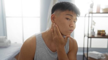 Yakışıklı genç Çinli bir adam, tenini içeride, sağlıklı yaşam için gerekli malzemelerle donatılmış sakin bir kaplıca odasında değerlendiriyor..