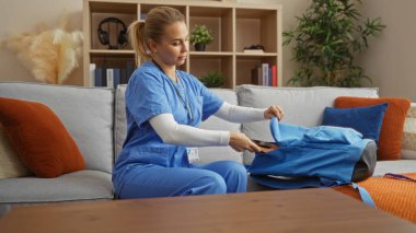 Önlüklü kadın çantalarını oturma odasındaki kanepeye koydu. Üzerinde modern dekor ve bitkiler vardı. Çalışmaya hazırlanıyordu..