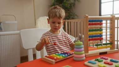 Çocuk evde renkli bir abaküs ve ksilofon içeren eğitici oyuncaklarla oynuyor. Kapalı mekanlar ve çocukluk anları sergiliyor.