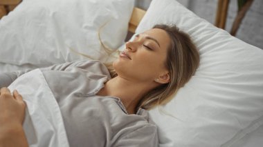 Kadın yatak odasının iç kısmında yumuşak yastıklarla huzur içinde uyuyor. Huzurlu bir ev ortamında huzurlu bir dinlenme anı yakalıyor..