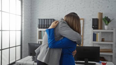 Bilgisayarlar ve raflarla çevrili bir ofis ortamında sarılan kadın ve erkek profesyonel bir ortamda samimiyet ve dostluk anlarını yakalıyorlar..