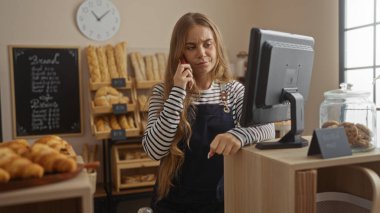 Fırında çalışan genç bir kadın kasada çalışırken telefonla konuşuyor.