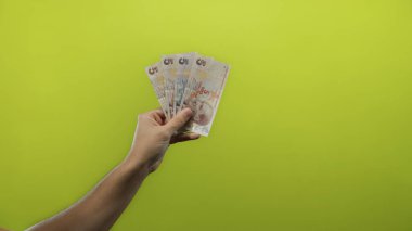 Elinde Türk lirası banknotları tutan bir adamın eli izole edilmiş sarı bir zemin üzerinde canlı bir finans teması oluşturuyor..