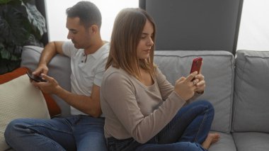 Çift rahat oturma odasındaki akıllı telefonları kullanarak rahat atmosferli evde modern ilişki dinamiklerini sergiliyor..